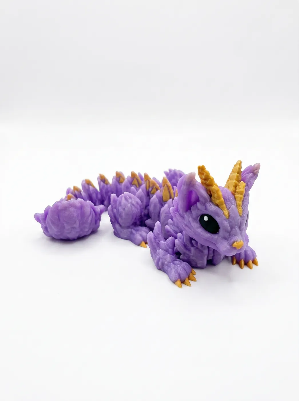 Purple 3D printed dragon with gold horns curled on a light studio surface.